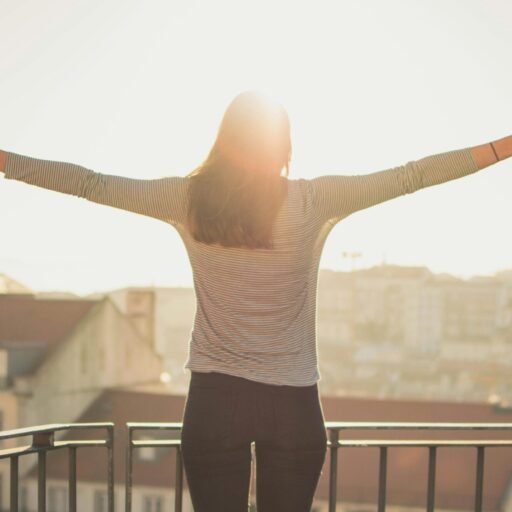 A woman stands with outstretched arms on a sunny balcony, embracing the morning light.